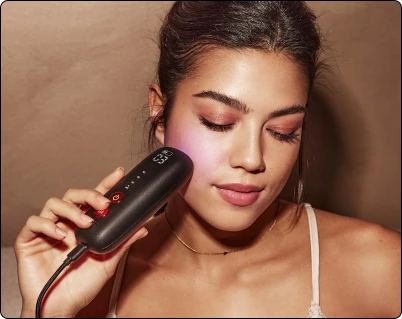 Жінка використовує чорний портативний пристрій світлотерапії Silk'n LED (світлодіод) на щоці.