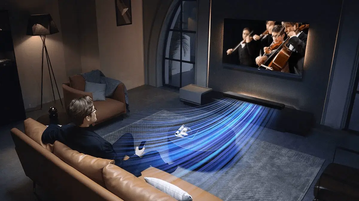 Чоловік на дивані у вітальні дивиться концерт струнних інструментів, саундбар TCL спрямовує звук на нього.