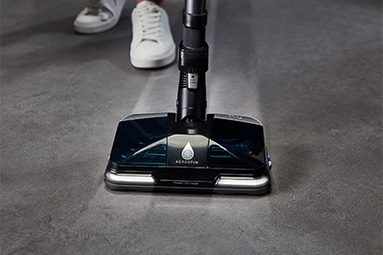 Пилосос Tefal X-Force Flex на сірій підлозі з увімкненим підсвічуванням. На задньому плані видно людське взуття.