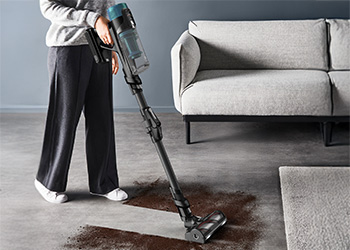 Людина тримає в руці пилосос Tefal X-Force Flex і висмоктує коричневий пісок із сірого килима.