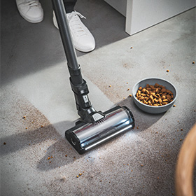 Крупний план пилососа Tefal X-Force Flex, який збирає розлиту їжу, а поруч стоїть миска з їжею.
