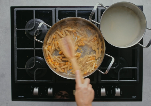 Людина помішує пасту в каструлі на газовій плиті GBC 75 VB VG.