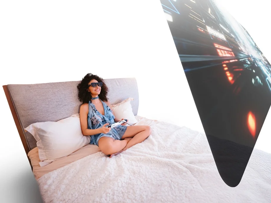 Жінка сидить на ліжку в окулярах XREAL One Pro і відображає перед собою віртуальний екран.