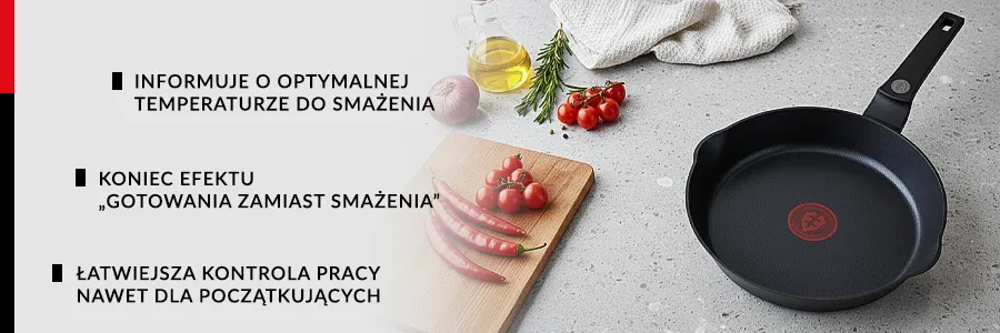 Patelnia na blacie kuchennym, obok leży deska do krojenia na której znajdują się papryczki oraz pomidorki koktailowe