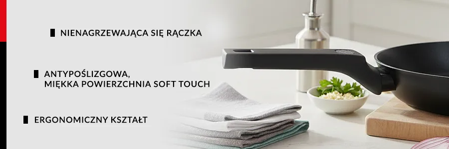 Przybliżenie na uchwyt patelni ZWIEGER KORRA, patelnia stoi na drwnianym podeście położonym na jasny blat kuchenny na którym leżą również ścierki i miska z przyprawami