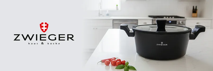 Czarny garnek KORRA stojacy na marmurowym blacie kuchennym, na blacie leży bazylia i pomidorki koktaliowe, w tle widać kuchnie ze zmywarką, kuchnią gazową oraz blokiem z nożami