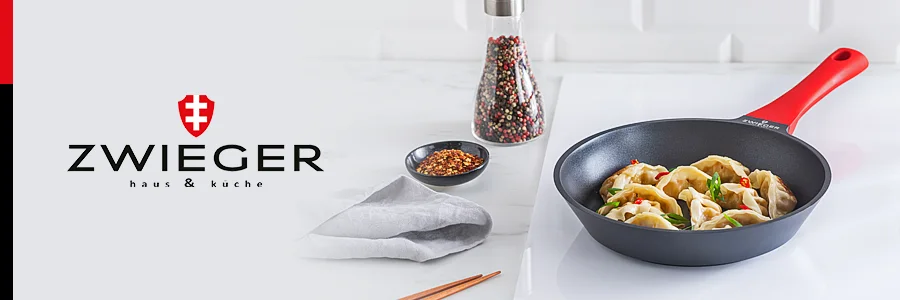 Patelnia z pierogami na jasnym blacie, obok stoi pieprzniczka i przyprawy