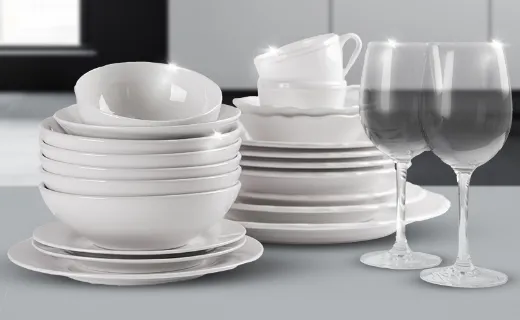 Крупний план стопки чистого посуду – тарілок, мисок, склянок та келихів – вишикуваних на кухонній стільниці.