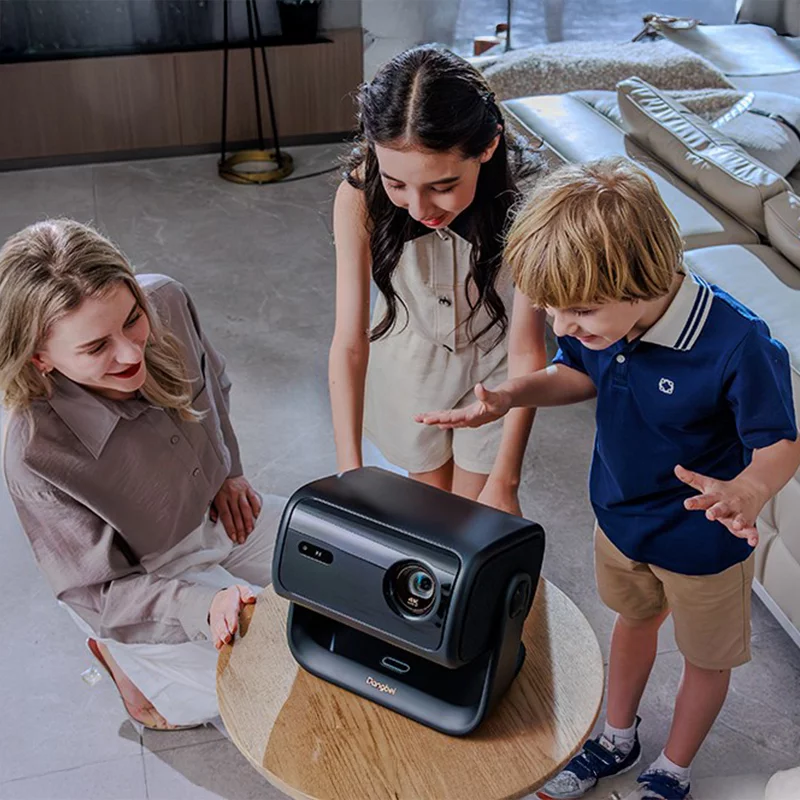 Жінка, дівчина та хлопець дивляться на проектор, що стоїть на столі.