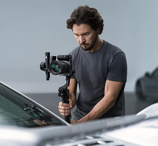 Чоловік у сірій футболці тримає стабілізатор DJI з прикріпленою камерою.