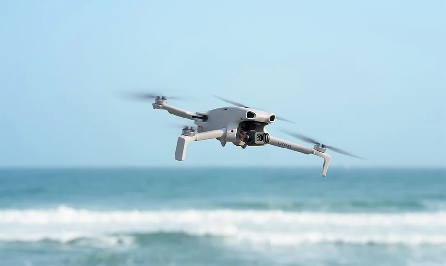 Szary dron DJI Lito X1 unoszący się stabilnie w powietrzu nad wzburzonymi wodami błękitnego oceanu