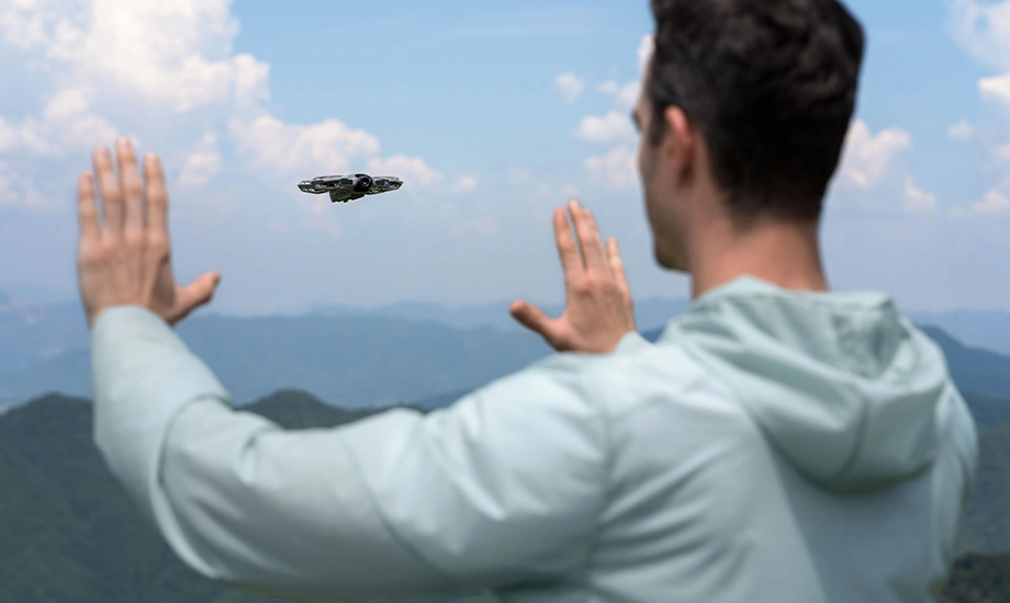 Чоловік використовує жести рук, щоб керувати літаючим дроном у горах.