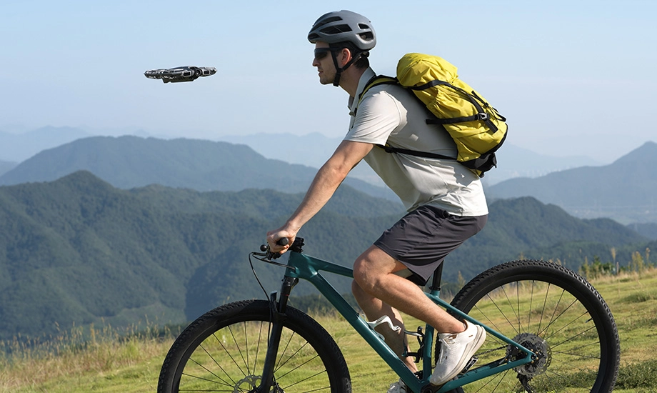 Чоловік їде на гірському велосипеді, а поруч з ним летить дрон.