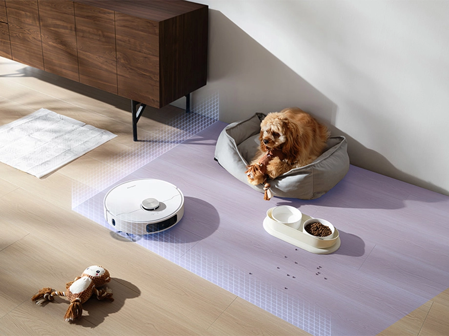 Робот моет пол в комнате, избегая собаку в постели, миски с едой и водой, а также игрушки.