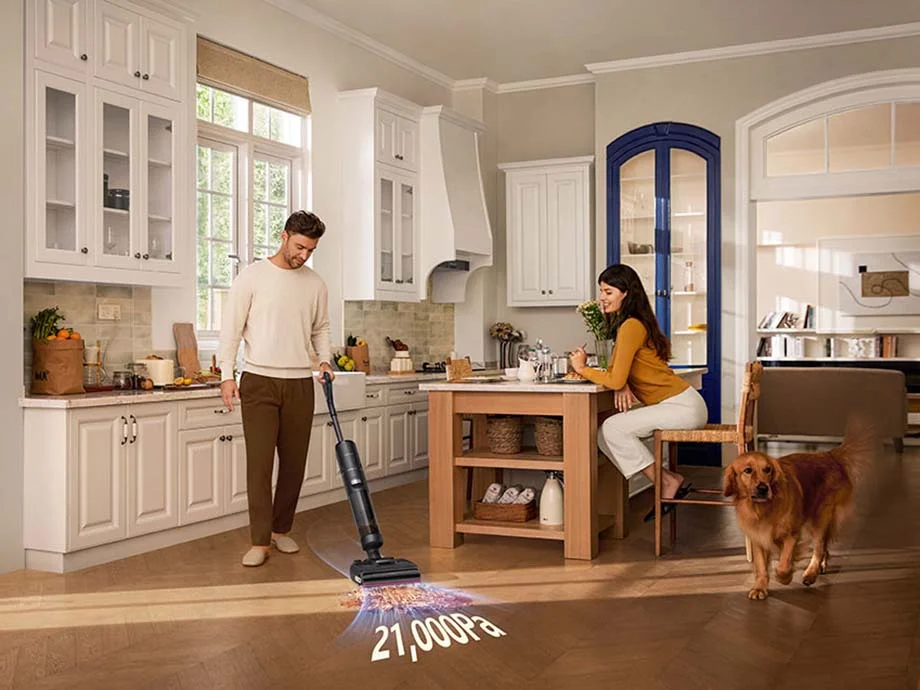 Чоловік пилососить підлогу на кухні, поруч стоять жінка та собака, а на підлозі показують 21 000 Па.