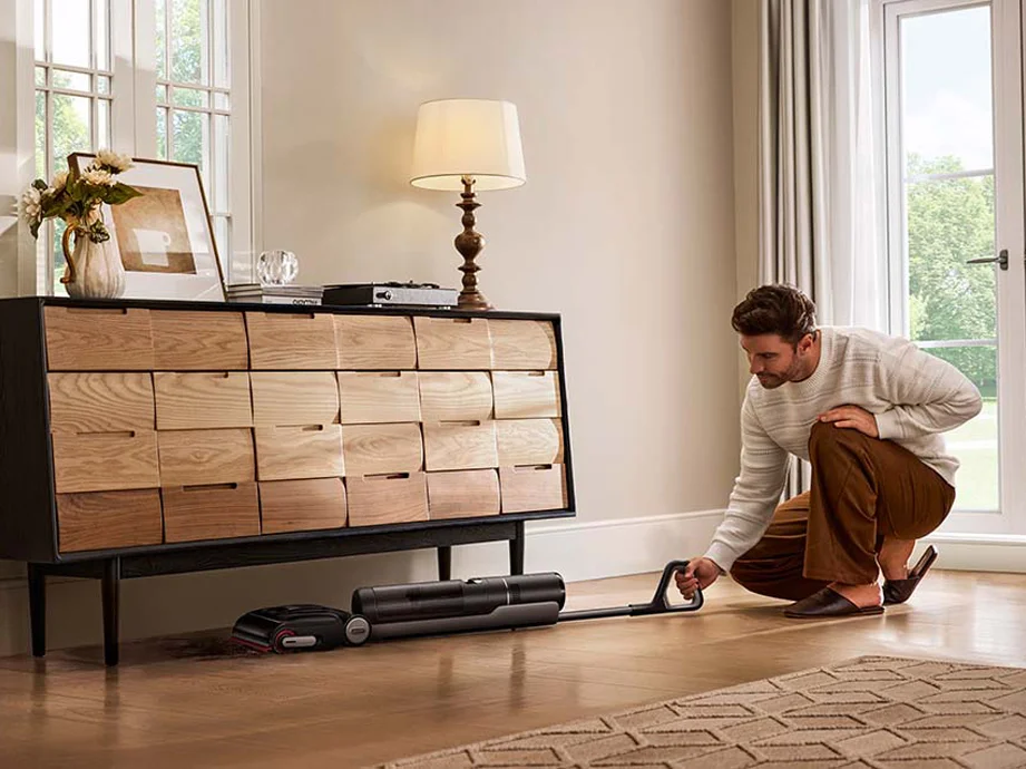 Чоловік пилососить підлогу вертикальним пилососом, розміщеним горизонтально.