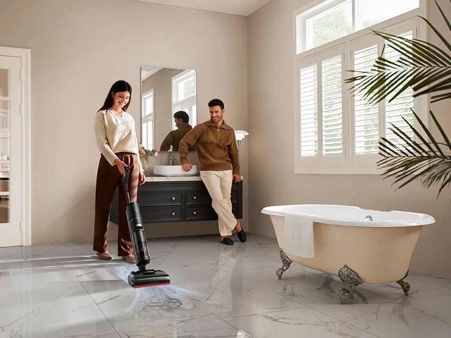 Жінка пилососить бруд з мармурової підлоги ванної кімнати, а поруч стоїть чоловік.