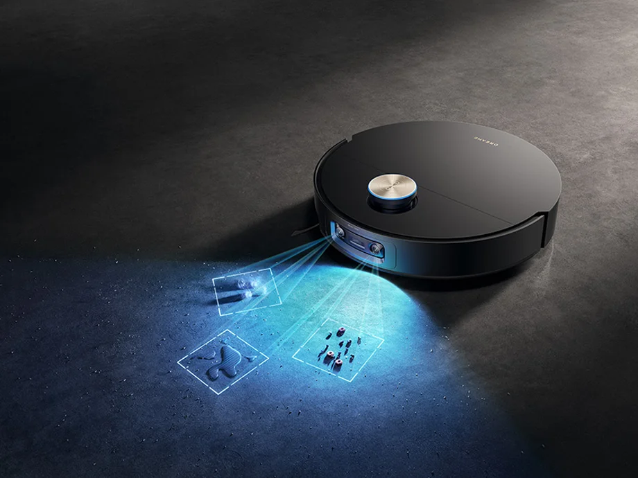 Чорний робот-пилосос виявляє та прибирає бруд у темній зоні, освітленій синім світлом.