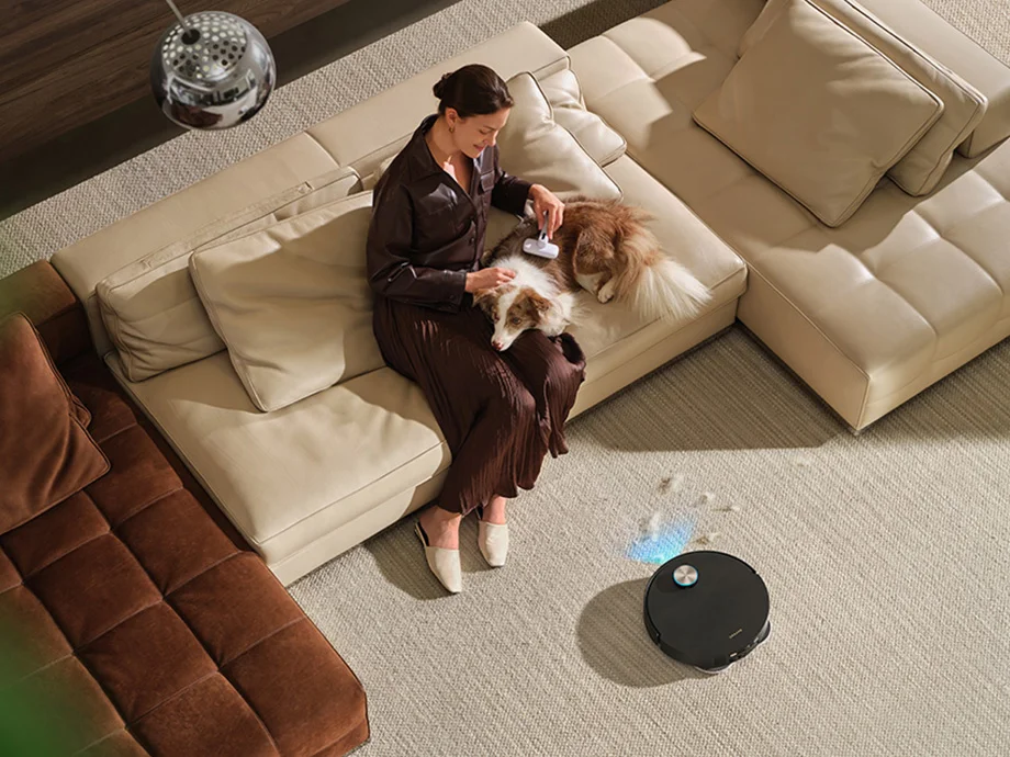 Чорний робот-прибиральник пилососить килим, поки жінка та її собака сидять на дивані.