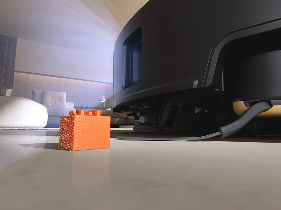 Крупний план чорного робота-пилососа, який пилососить підлогу, уникаючи іграшок.