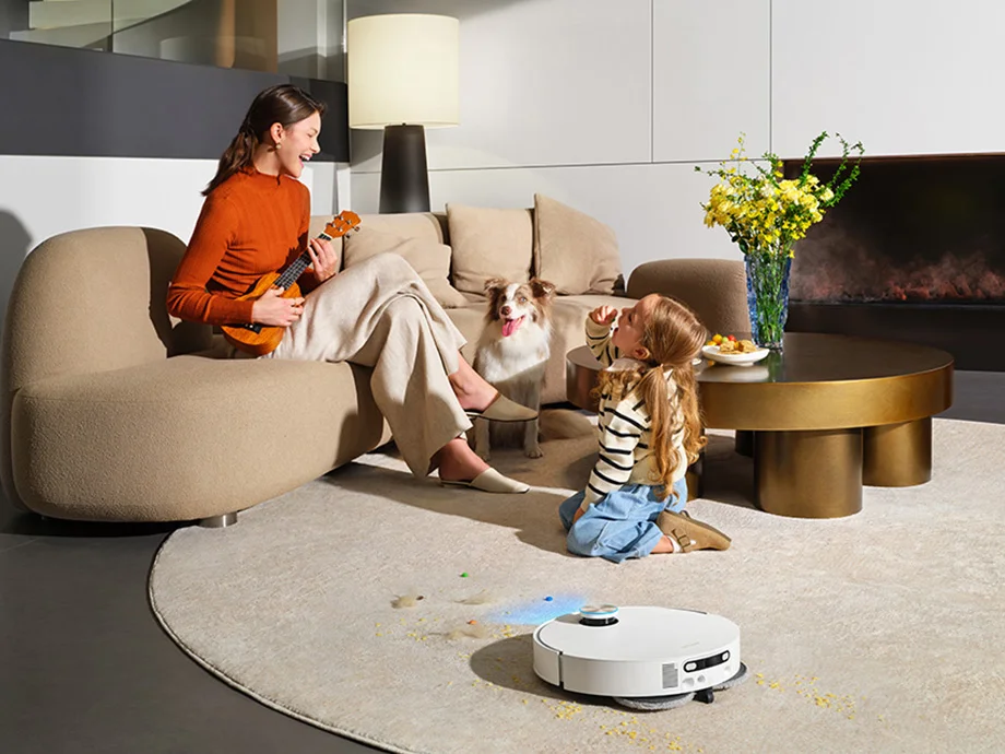 Мати та її донька проводять час разом у світлій, сучасній вітальні, а поруч робот чистить килим.