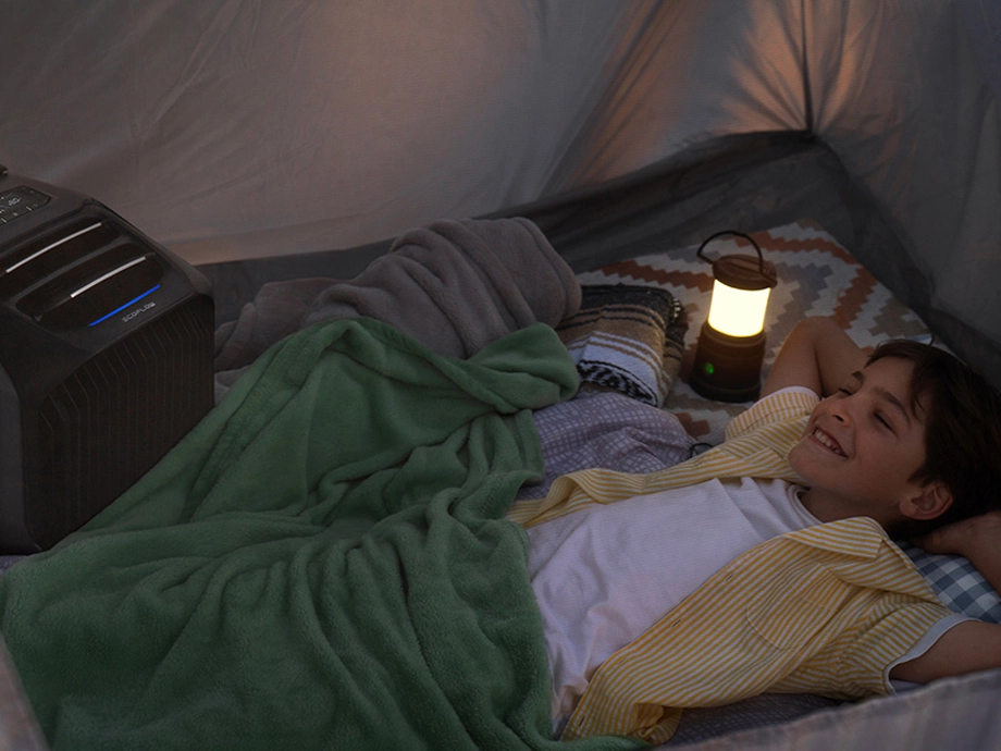 Хлопчик лежить під ковдрою в наметі. Поруч з ним горить лампа та працює кондиціонер.