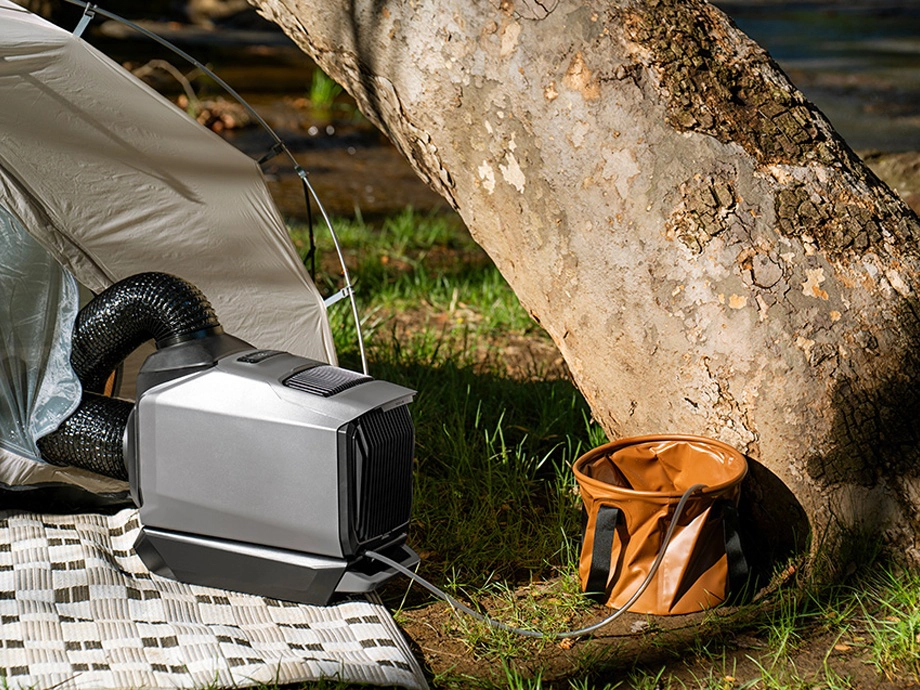 Кондиціонер стоїть поруч із наметом. Праворуч під ним видно дерево та резервуар для води.