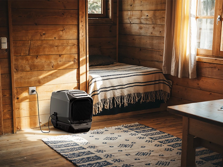 Кондиціонер підключено до розетки в дерев'яному будинку. Поруч видно ліжко, вікно та стіл.