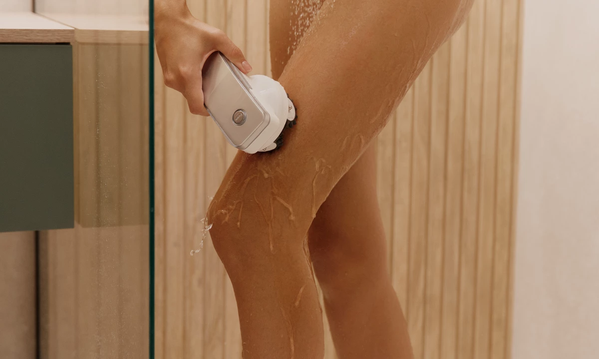 Крупний план жіночої ноги в душі, яку масажують за допомогою приладу Garett Beauty Cellu Body.