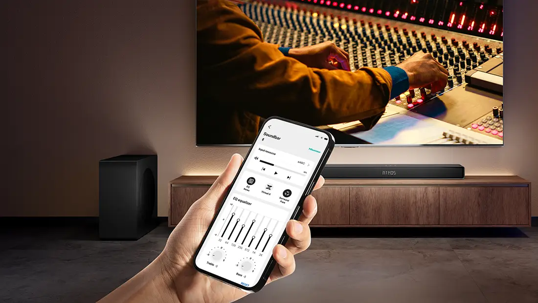 Смартфон із застосунком для керування саундбаром AX3120Q тримають перед телевізором, а саундбар — на шафі.