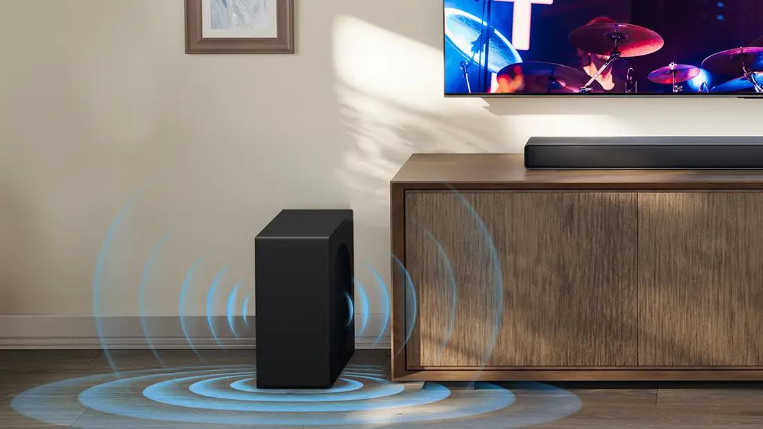 Чорний саундбар і сабвуфер розташовані поруч із дерев'яною шафою, а на телевізорі транслюється концерт.