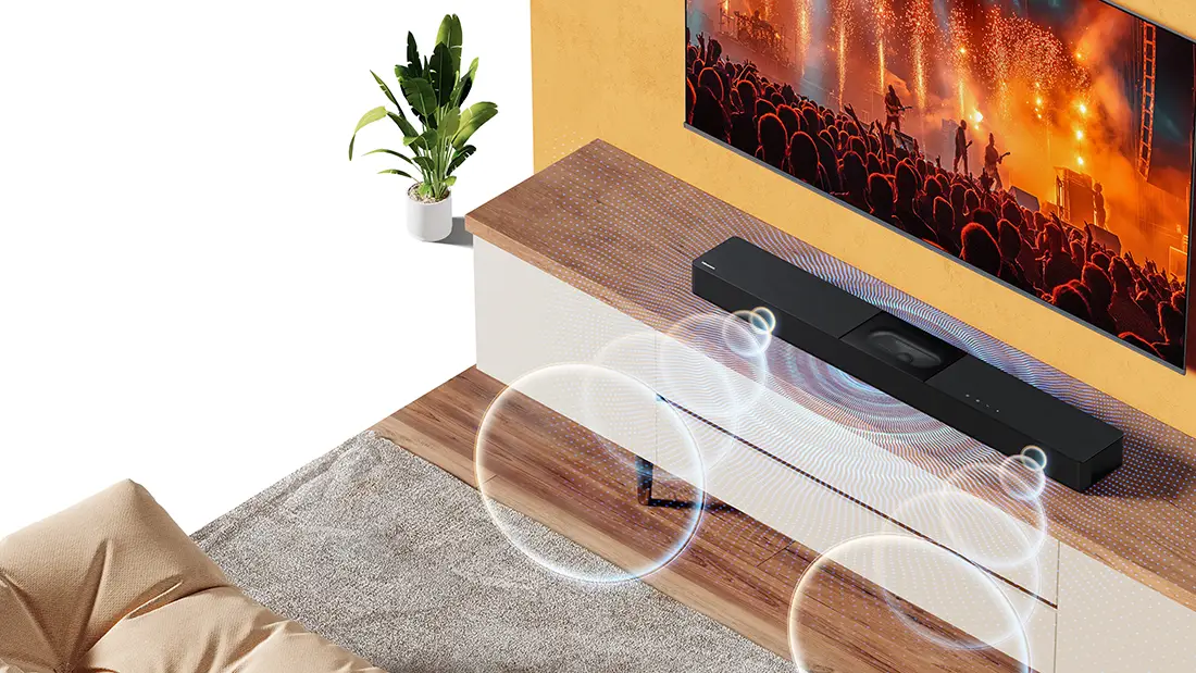 Саундбар, розміщений на дерев'яній шафі під телевізором, поруч із ним зелена рослина в білому горщику.