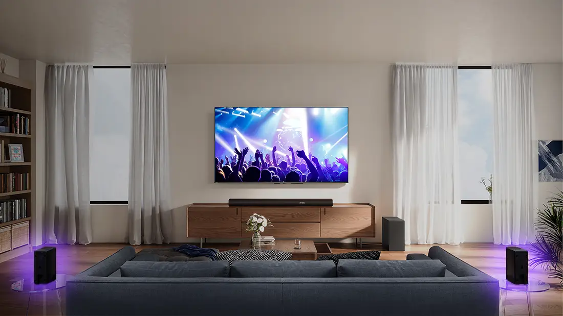 Телевізор на стіні з концертною музикою, саундбар на шафі, два динаміки з фіолетовим підсвічуванням з боків.