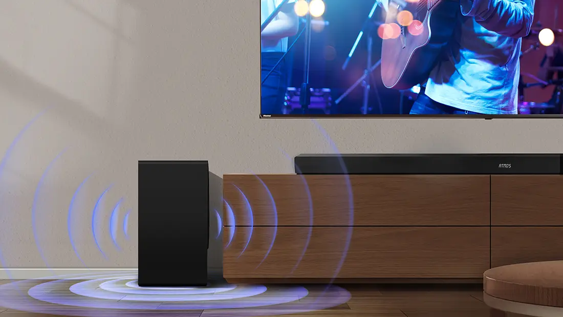 Чорний саундбар стоїть на дерев'яній шафі поруч із сабвуфером із синіми звуковими хвилями.