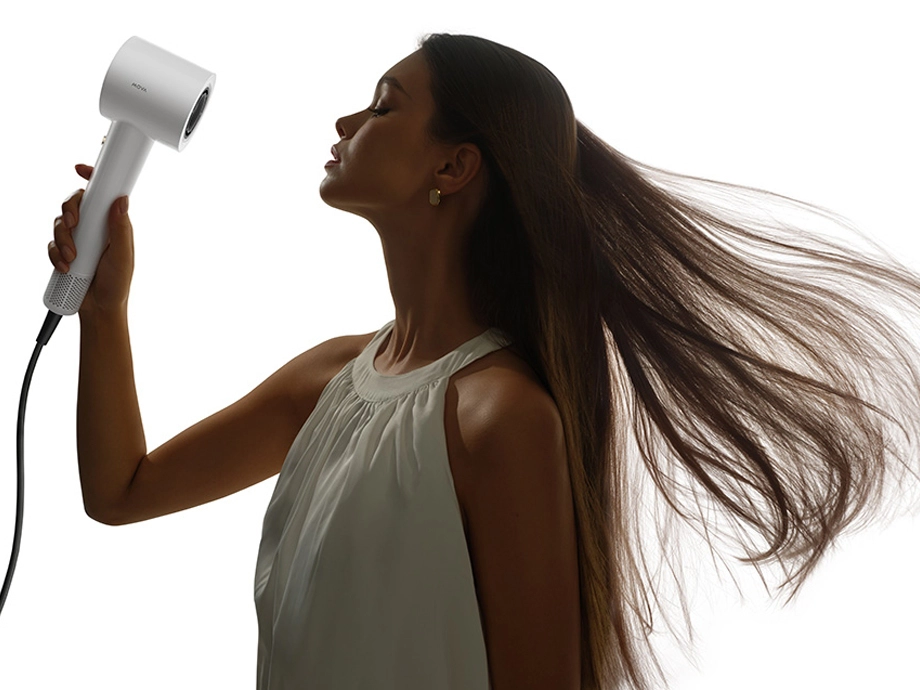Жінка в білій блузці сушить волосся білою сушаркою MOVA з розпущеним волоссям