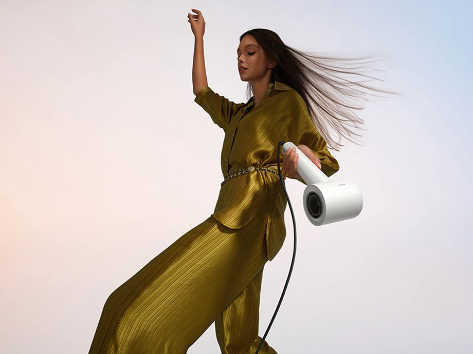 Жінка в золотій сукні тримає білий фен з розпущеним волоссям