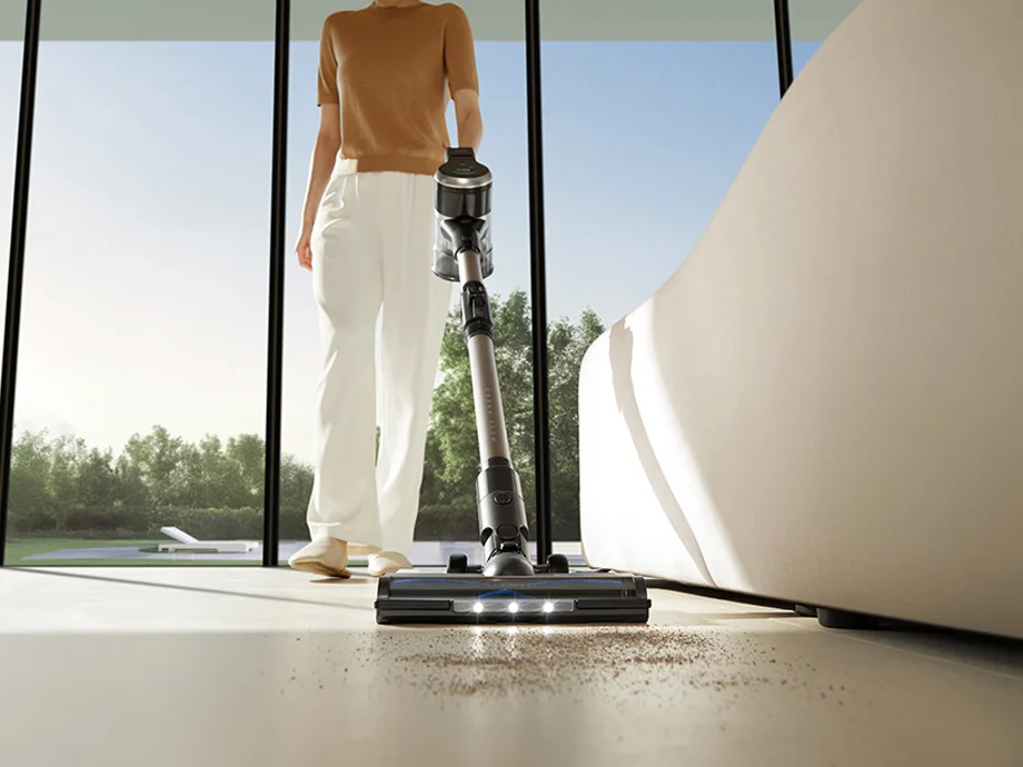 жінка пилососить підлогу бездротовим пилососом біля великого вікна