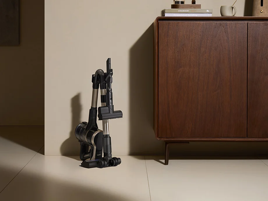 складений пилосос, що стоїть вертикально поруч із дерев'яною комодою