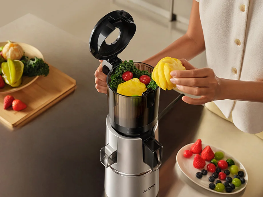 Жінка додає шматочки ананаса у відкриту соковижималку на кухонному столі.