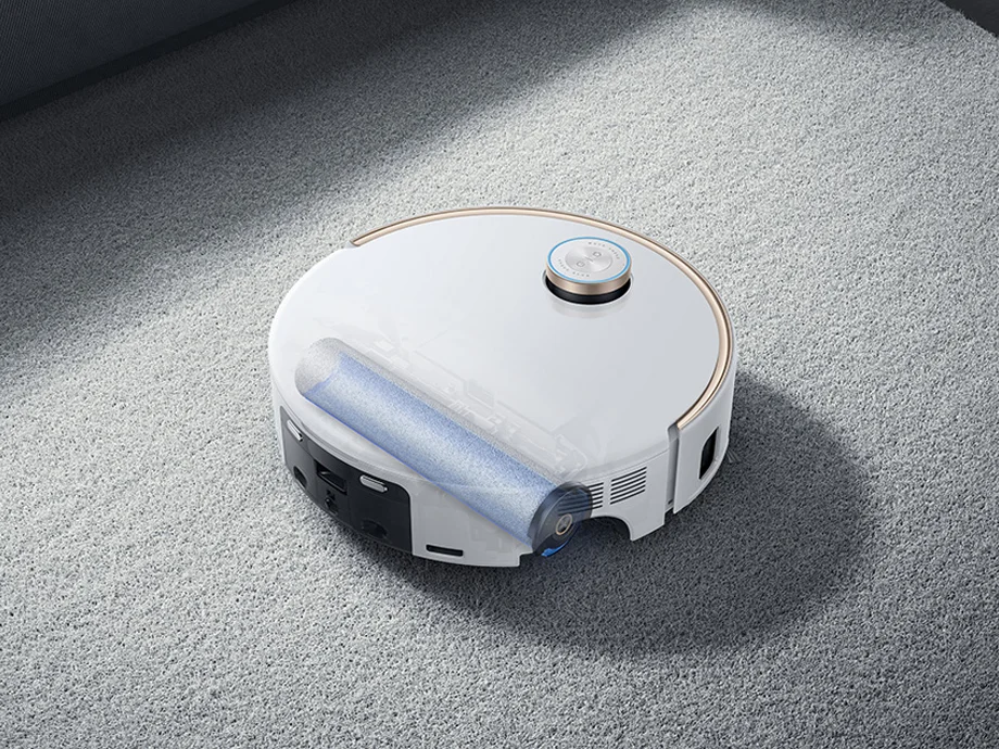 Білий роботизований пилосос на килимі з видимим роликом для чищення.