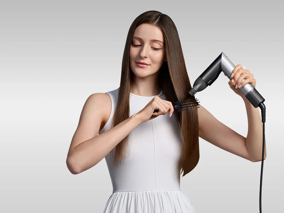 Жінка укладає своє довге волосся щіткою та феном у мінімалістичній студії.