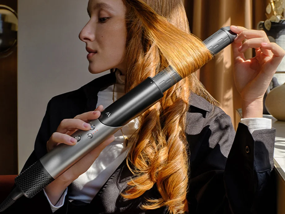 Жінка укладає своє довге волосся плойкою