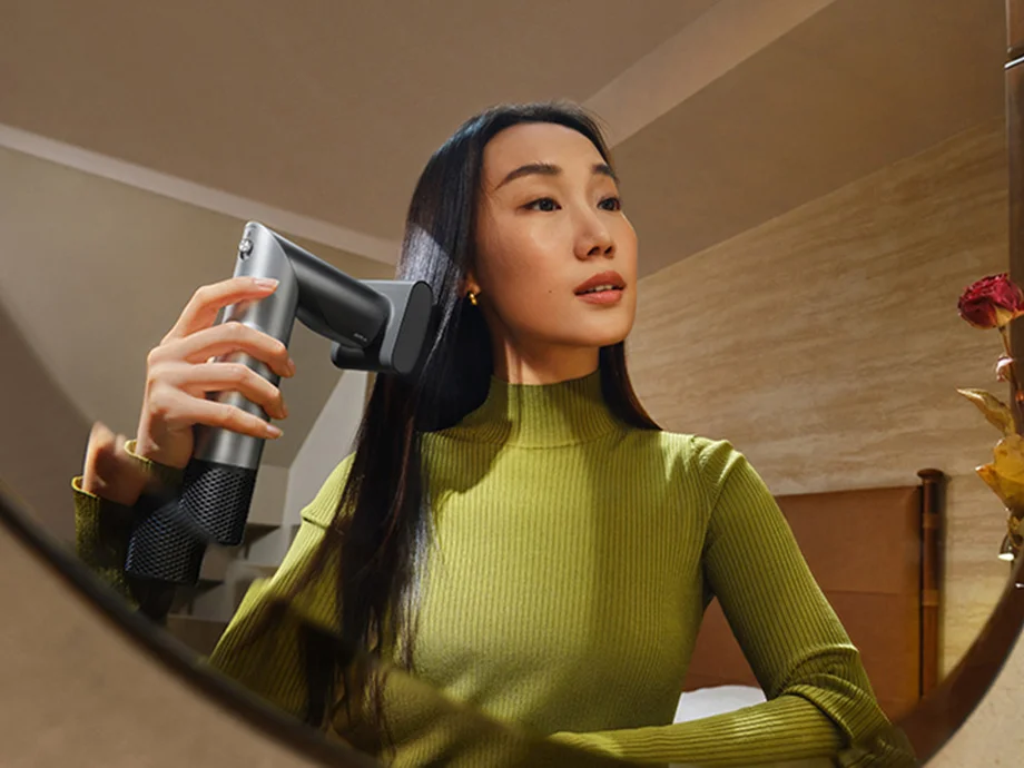 Жінка сушить волосся феном, дивлячись у дзеркало у своїй спальні.