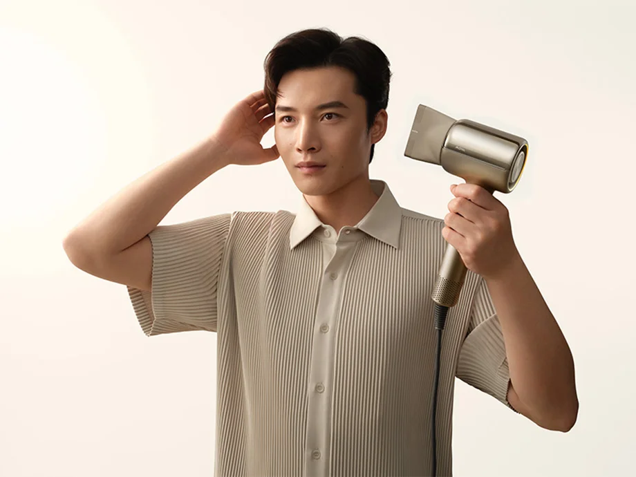 Чоловік тримає фен, а іншою рукою торкається голови.