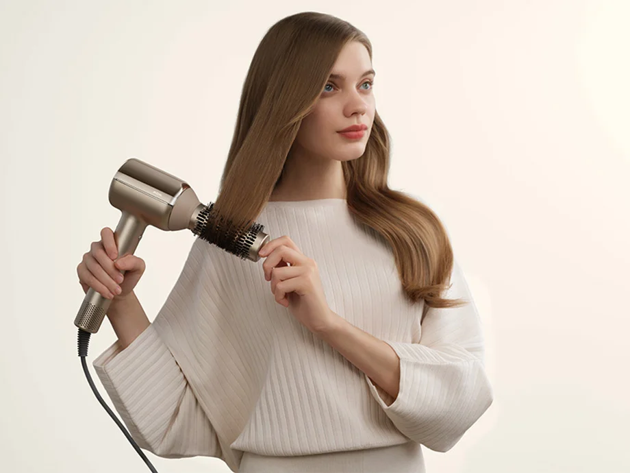 Жінка укладає своє довге волосся феном і круглою щіткою.
