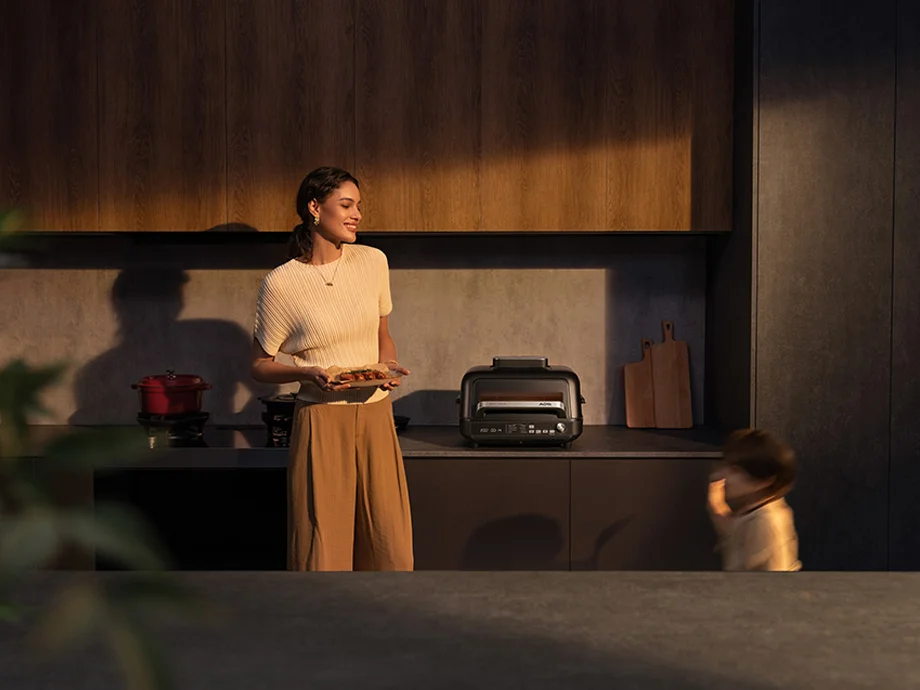 Жінка тримає тарілку з їжею та дивиться на дитину, яка проходить повз кухонну стільницю з пристроєм MOVA.