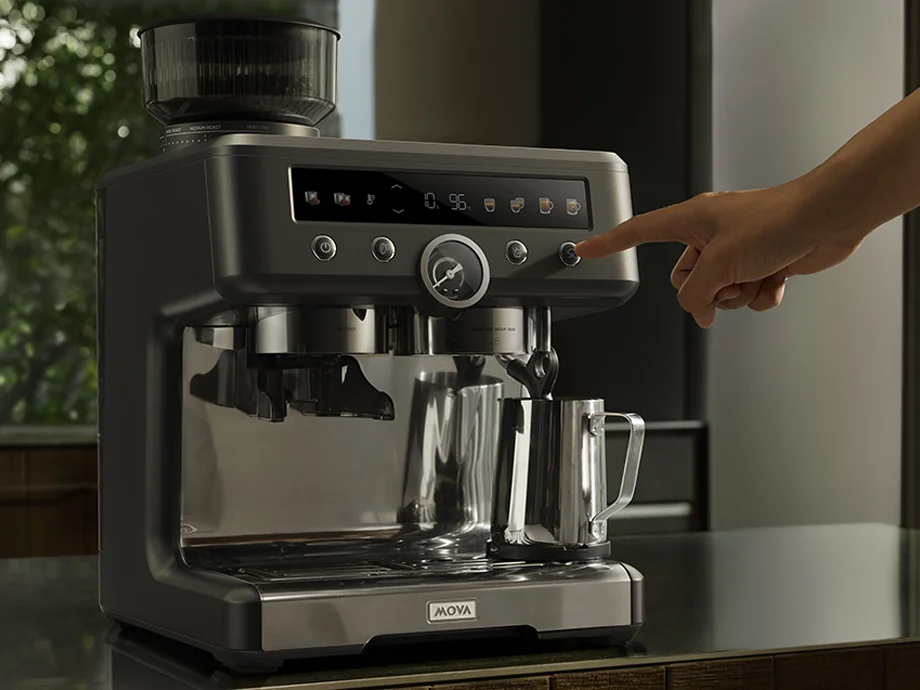 Рука натискає кнопку на панелі кавоварки з металевим глечиком на підносі.
