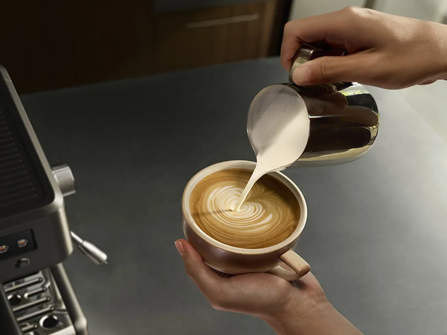Крупний план рук, що наливають молоко в чашку лате з видимим візерунком на піні