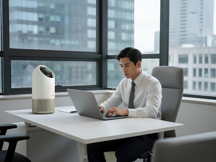 Чоловік працює за столом, поруч з ним очищувач повітря, а за вікном вид на місто.