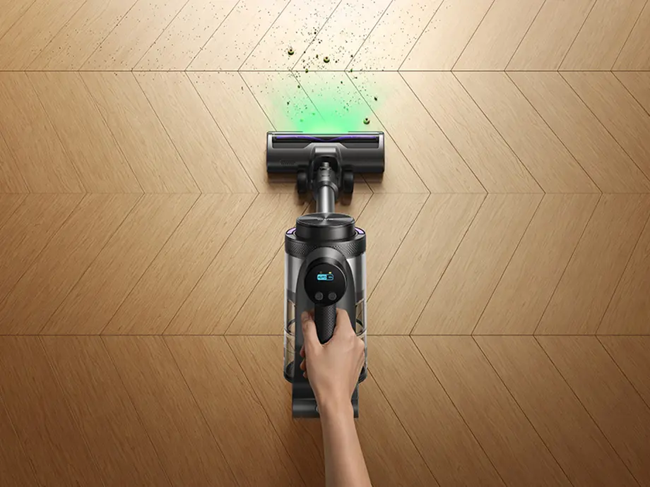Top view of a hand holding an upright vacuum cleaner vacuuming a dirty floor.